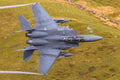 Gray fighter jet flying over a green landscape