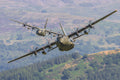 Military aircraft flying over a landscape with green hills and trees