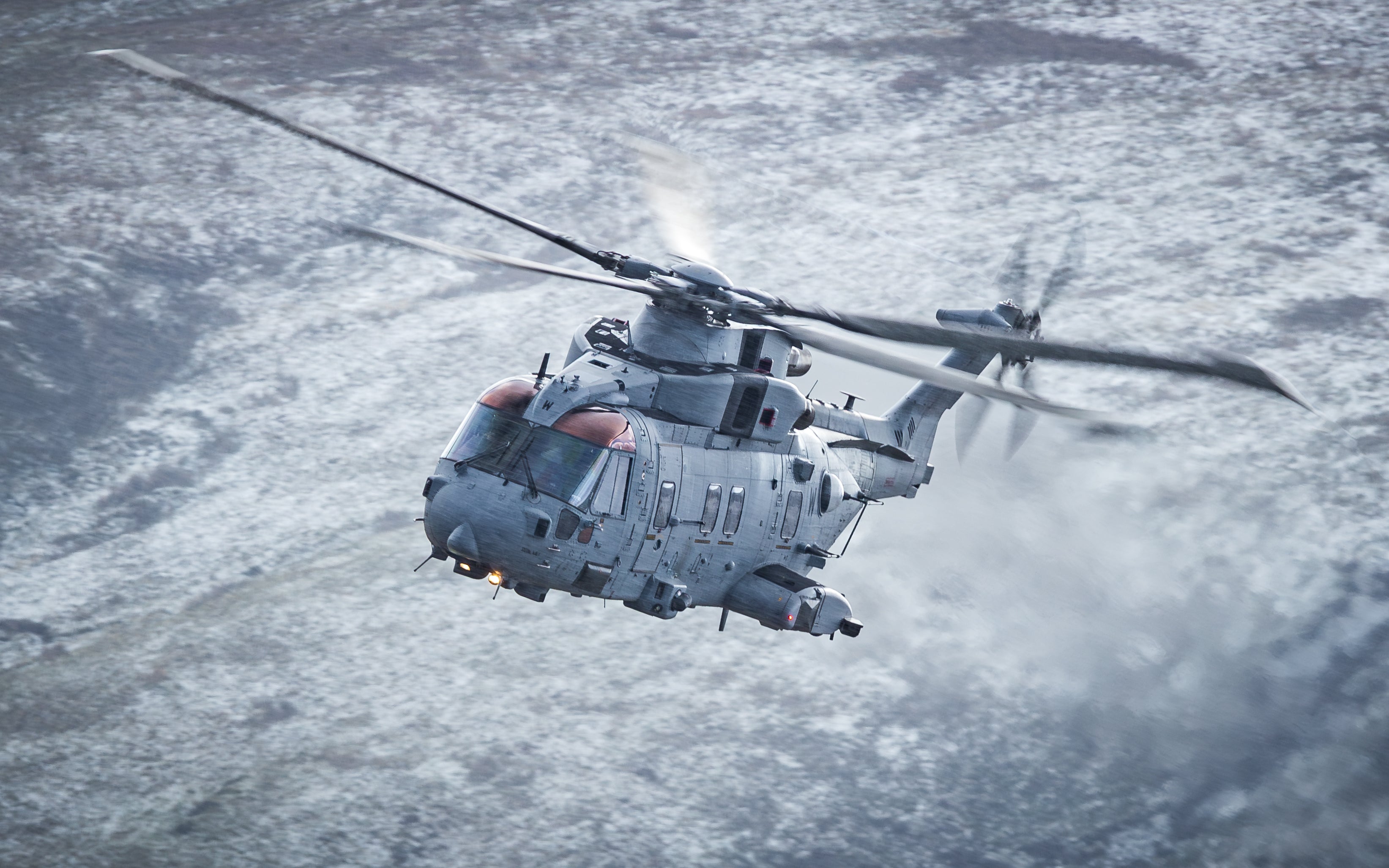 Military helicopter flying over snow covered hills